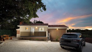 Una casa moderna con entrada de vehículos, un automóvil estacionado al frente y un banco a la izquierda.