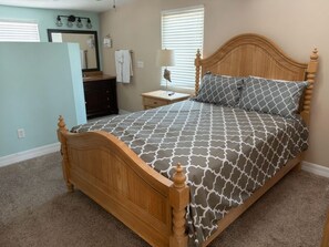 Una camera da letto con un letto in legno, un comodino, una lampada, uno specchio e un bagno con un porta asciugamani.
