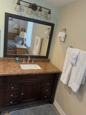 A bathroom with a granite countertop sink, dark wooden vanity, a large mirror, and two towels on hooks. - 2-bedroom apartment in pleasant Fort Myers Beach with AC (Fort Myers Beach)