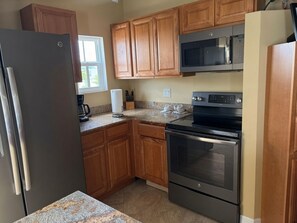 A kitchen with wooden cabinets, a stainless steel refrigerator, a microwave, an oven, and a granite countertop. - 2-bedroom apartment in pleasant Fort Myers Beach with AC (Fort Myers Beach)