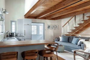 Eine moderne Küche mit Holzbalken, einem Essbereich mit Barhocker, einem grauen Sofa und einer Treppe.