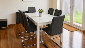 A modern dining area with a white table, black chairs, a potted plant, and a framed artwork on the wall. - Chic 5Bed City Centre Home-Sleeps9-Near QMC&Castle (Nottingham)