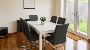 A modern dining area with a white table, black chairs, a potted plant, and a framed artwork on the wall.