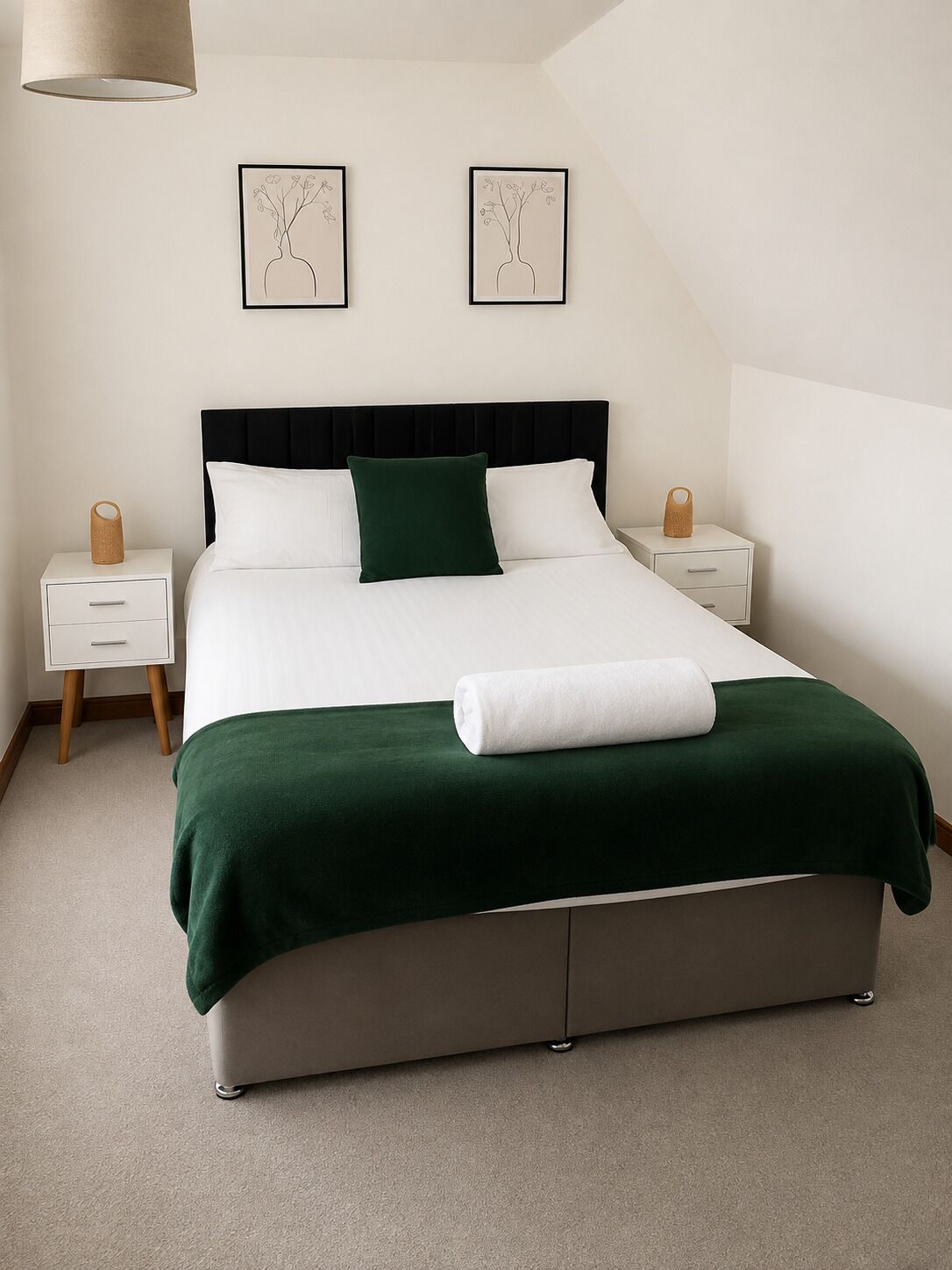 A bedroom with a bed, two bedside tables, a lamp, and two wall-mounted pictures.