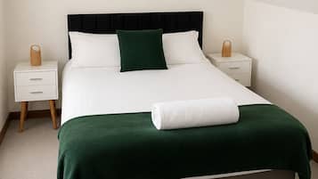 A bedroom with a bed, two bedside tables, a lamp, and two wall-mounted pictures.