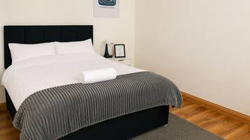 A neatly made bed with a black headboard, a grey striped blanket, and a white pillow.