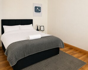 En pænt redt seng med sort sengegavl, gråt stribet tæppe og hvid pude.