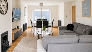 A modern living room with a grey sofa, a TV, a fireplace, and a dining area with chairs and a table. - Chic 5Bed City Centre Home-Sleeps9-Near QMC&Castle (Nottingham)