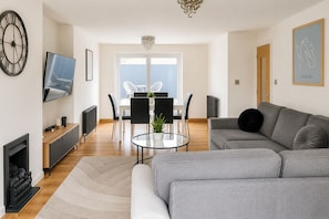 En moderne stue med en grå sofa, et fjernsyn, en pejs og et spiseområde med stole og et bord.