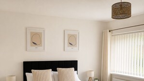 A neatly made bed with a black headboard, two framed artworks on the wall, and a window with blinds. - Chic 5Bed City Centre Home-Sleeps9-Near QMC&Castle (Nottingham)