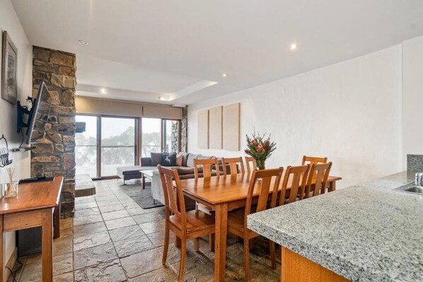 A modern kitchen with granite countertops, a dining area with wooden chairs, and a stone fireplace.