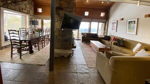 A spacious living area with a stone fireplace, a television, a sofa, and a dining table with chairs. - Alpine Woodsmoke  (Falls Creek)