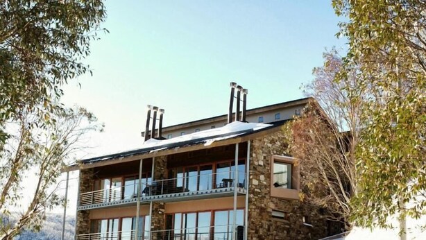 A multi-story building with balconies, stone facade, and a parked car in the snow. - Alpine Woodsmoke  (Falls Creek)
