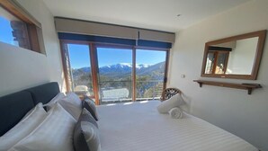 A hotel room with a large bed, a balcony with a mountain view, and a mirror on the wall. - Alpine Woodsmoke  (Falls Creek)