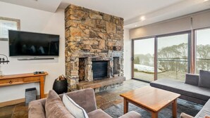 A living room with a stone fireplace, a flat-screen TV, a sofa, and a coffee table. - Alpine Woodsmoke  (Falls Creek)