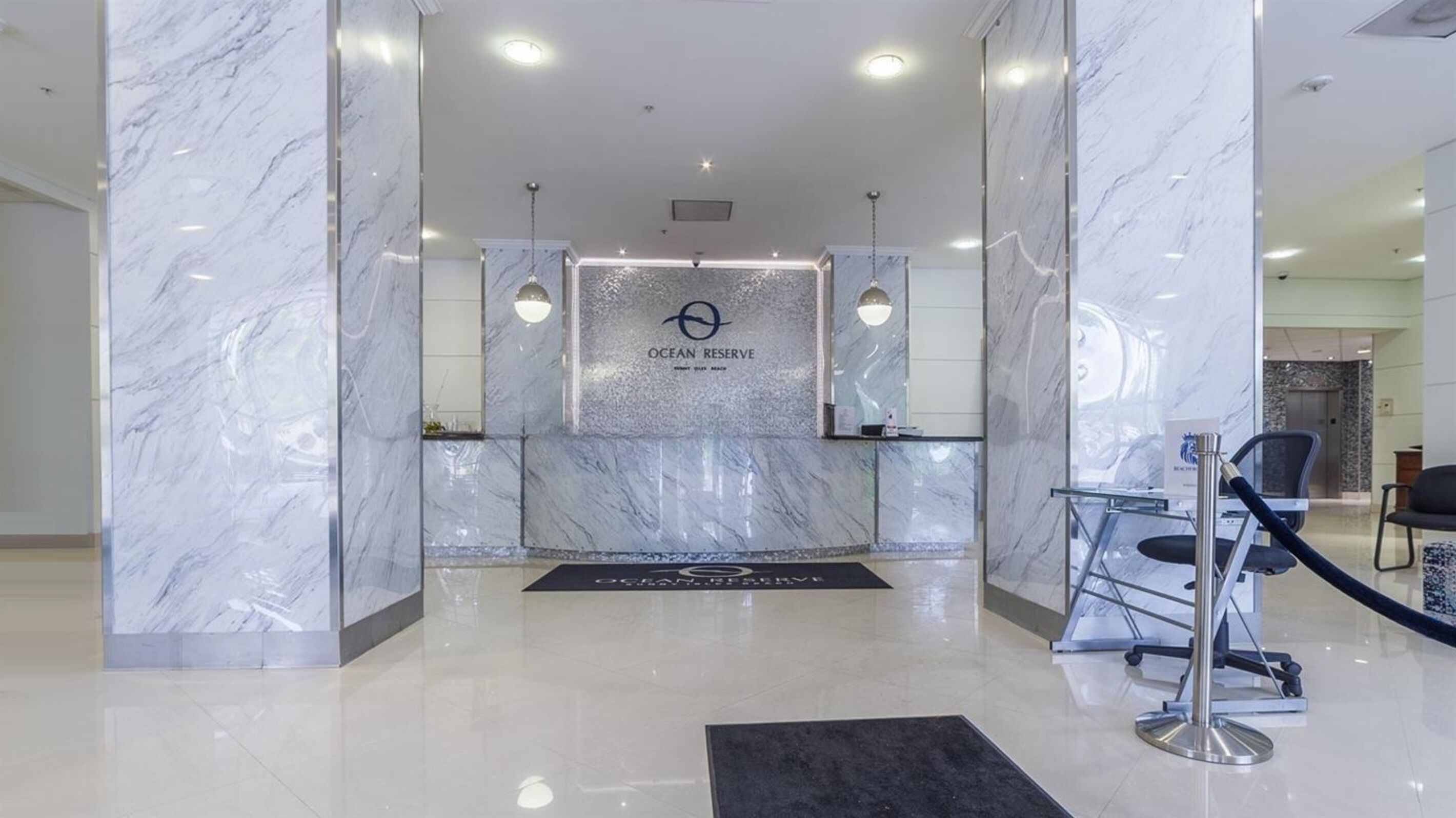 A reception area with marble walls, a reception desk, and a seating area with a chair and a black mat.