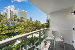 A balcony with a view of a cityscape, a white chair, and a small table with a plant. - Walk to Ocean | Luxury 2BR w/ King Master & Pool (Sunny Isles Beach)