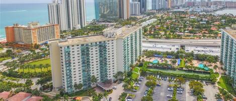 A high-rise hotel with multiple floors, a parking lot, and a view of the ocean and city skyline.