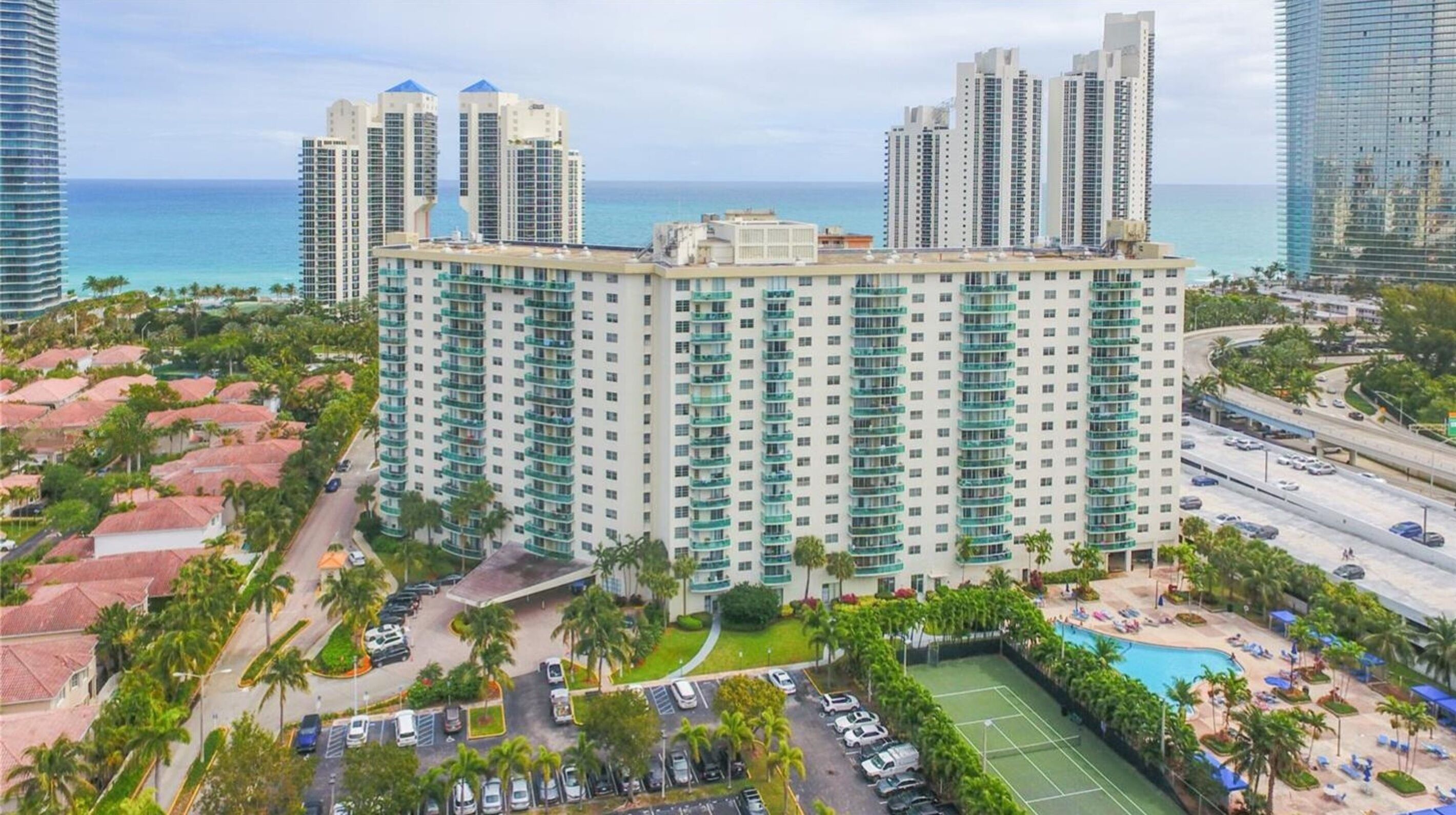 Un hotel moderno de gran altura con varias plantas, piscina y cancha de tenis.