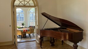 A grand piano in a spacious room with a herringbone floor and a large arched doorway leading to a dining area. - Historic Copenhagen Villa with Garden (København)
