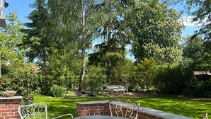 An outdoor patio with a round table and metal chairs, surrounded by a brick wall and greenery. - Historic Copenhagen Villa with Garden (København)