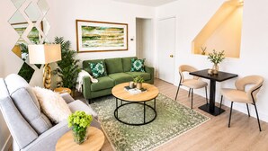 Ein modernes Wohnzimmer mit einem grünen Sofa, einem grauen Sessel, einem runden Couchtisch und einem Essbereich mit Tisch und Stühlen.