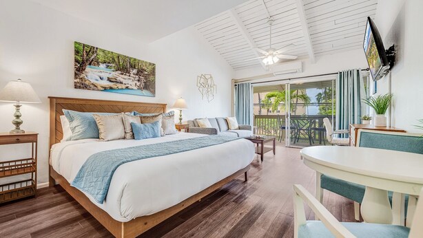 Ein Hotelzimmer mit einem großen Bett, einem Balkon mit Blick, einem an der Wand montierten Fernseher und einem Deckenventilator.
