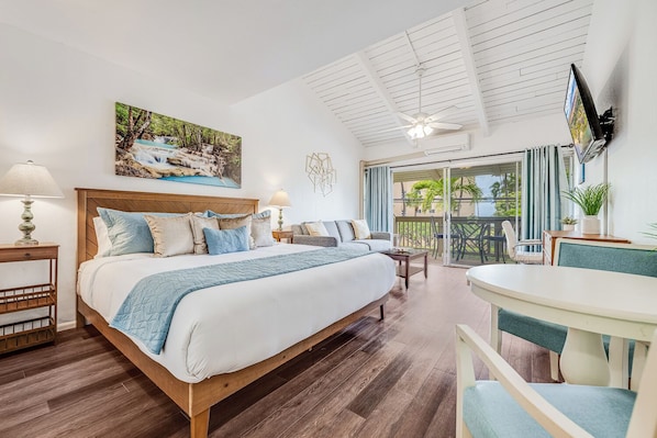 Ein Hotelzimmer mit einem großen Bett, einem Balkon mit Blick, einem an der Wand montierten Fernseher und einem Deckenventilator.