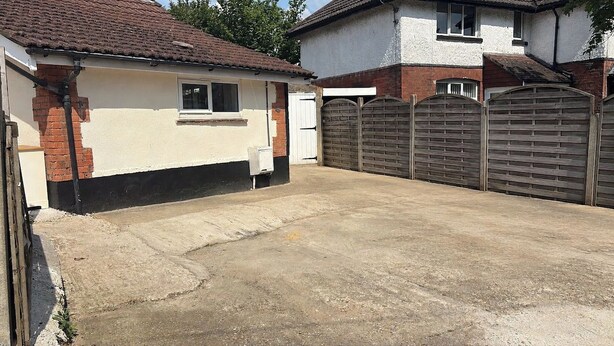 Eine Garage mit Wohnnutzung, einem Betonboden, einer Ziegelwand und einem Holztor.