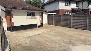 A residential garage with a concrete floor, a brick wall, and a wooden gate. - Modern Bungalow with Parking for 2 | Long Stays (Southampton)