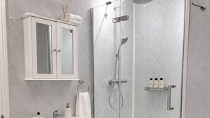 Un baño moderno con ducha envuelta en vidrio, tocador blanco con espejo y una pequeña cesta de mimbre con toallas.