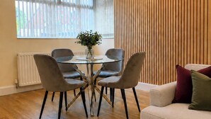 Ein modernes Wohnzimmer mit Essbereich, mit Holzboden, einer Couch mit Kissen und einem Tisch mit Stühlen.