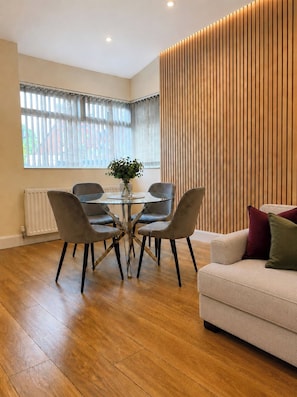 Ein modernes Wohnzimmer mit Essbereich, mit Holzboden, einer Couch mit Kissen und einem Tisch mit Stühlen.