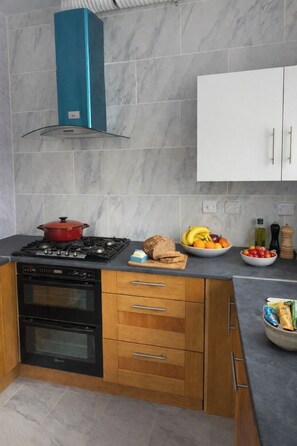 Eine moderne Küche mit Gasherd, Backofen, Holzschränken, Marmorfliesenspiegel und einem weißen Schrank.
