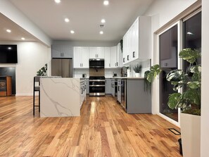 A modern kitchen with white cabinets, stainless steel appliances, and wooden flooring. - Luxury Retreat with Heated pool, sauna and jacuzzi (Covington township)