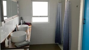 Une salle de bain avec un grand miroir, deux lavabos, une fenêtre et un rideau de douche.