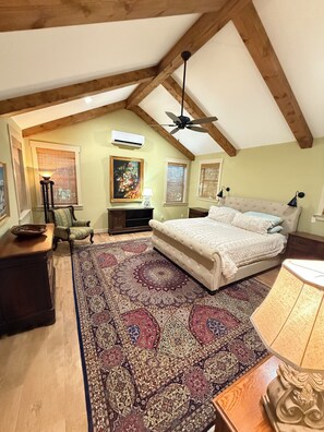 Un dormitorio con una cama grande, un ventilador de techo, una ventana con persianas y una alfombra decorativa.