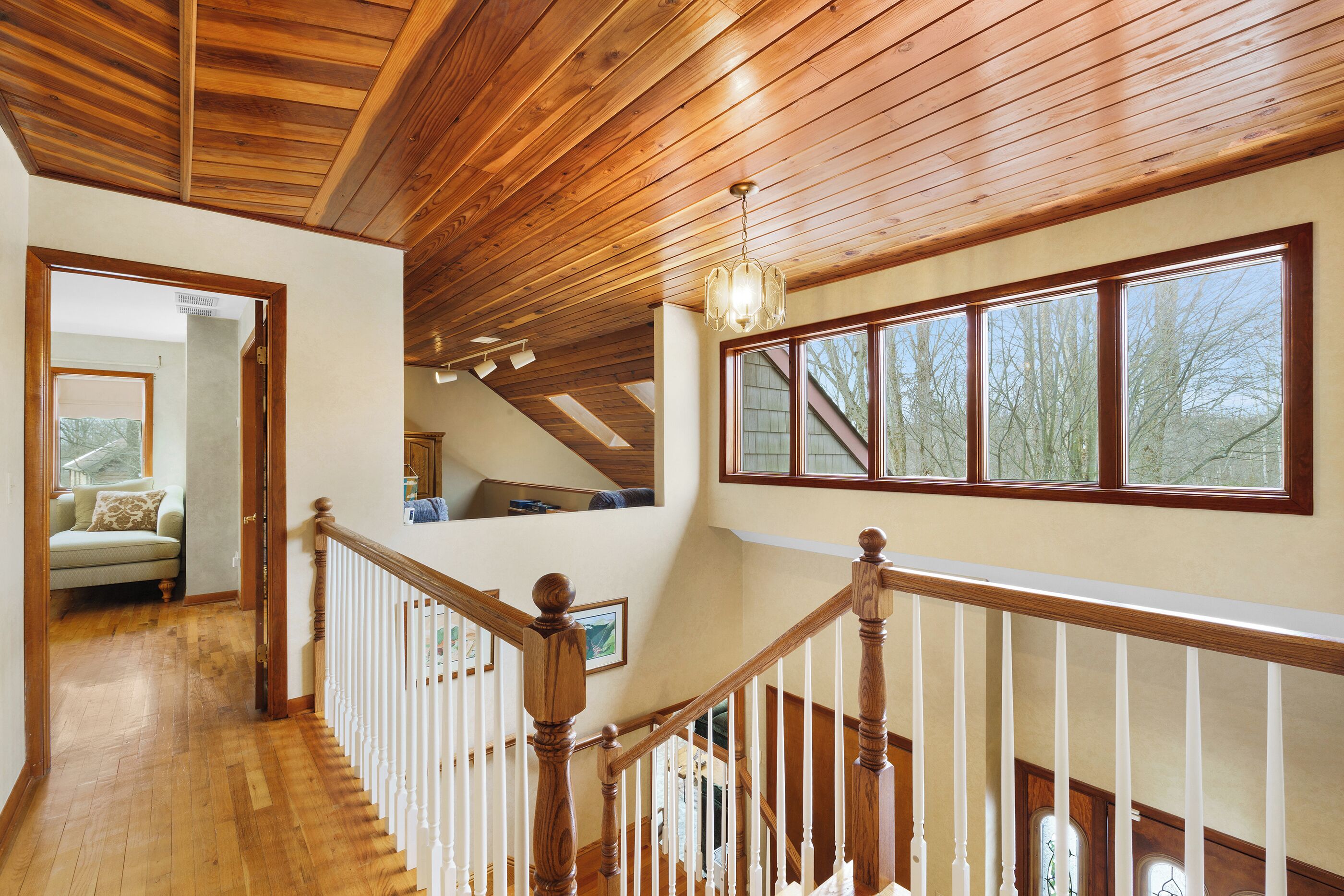 View from the stairs of the primary bedroom door and open loft above the living room. Natural light pours in through large windows and skylights. The bedroom is visually private, though sound and light can travel between spaces.