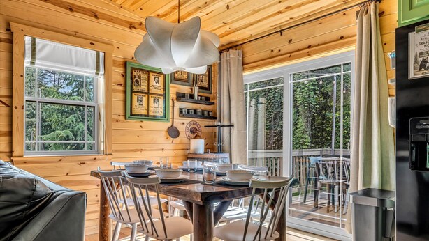 A wooden cabin interior with a dining table set, wooden walls, and large windows. - Dollywood Escape | Hot Tub • Fire Pit • Arcade (Pigeon Forge)