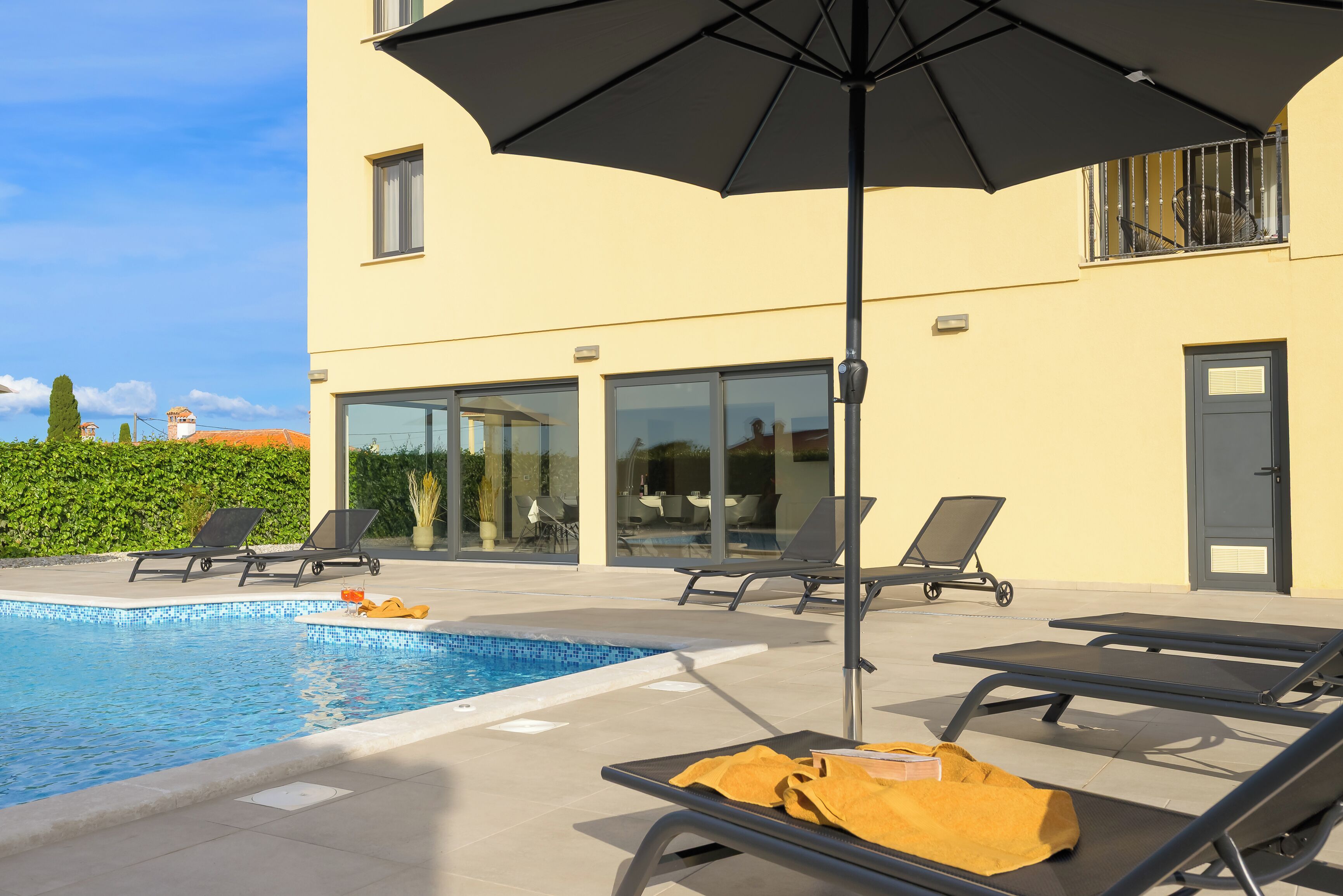 A swimming pool with lounge chairs and an umbrella, a building with large windows, and a door.