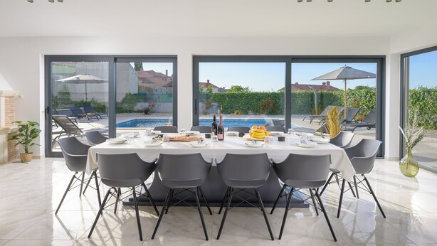 Ein Essbereich mit einem Tisch für sechs Personen, großen Fenstern und Blick auf einen Pool.