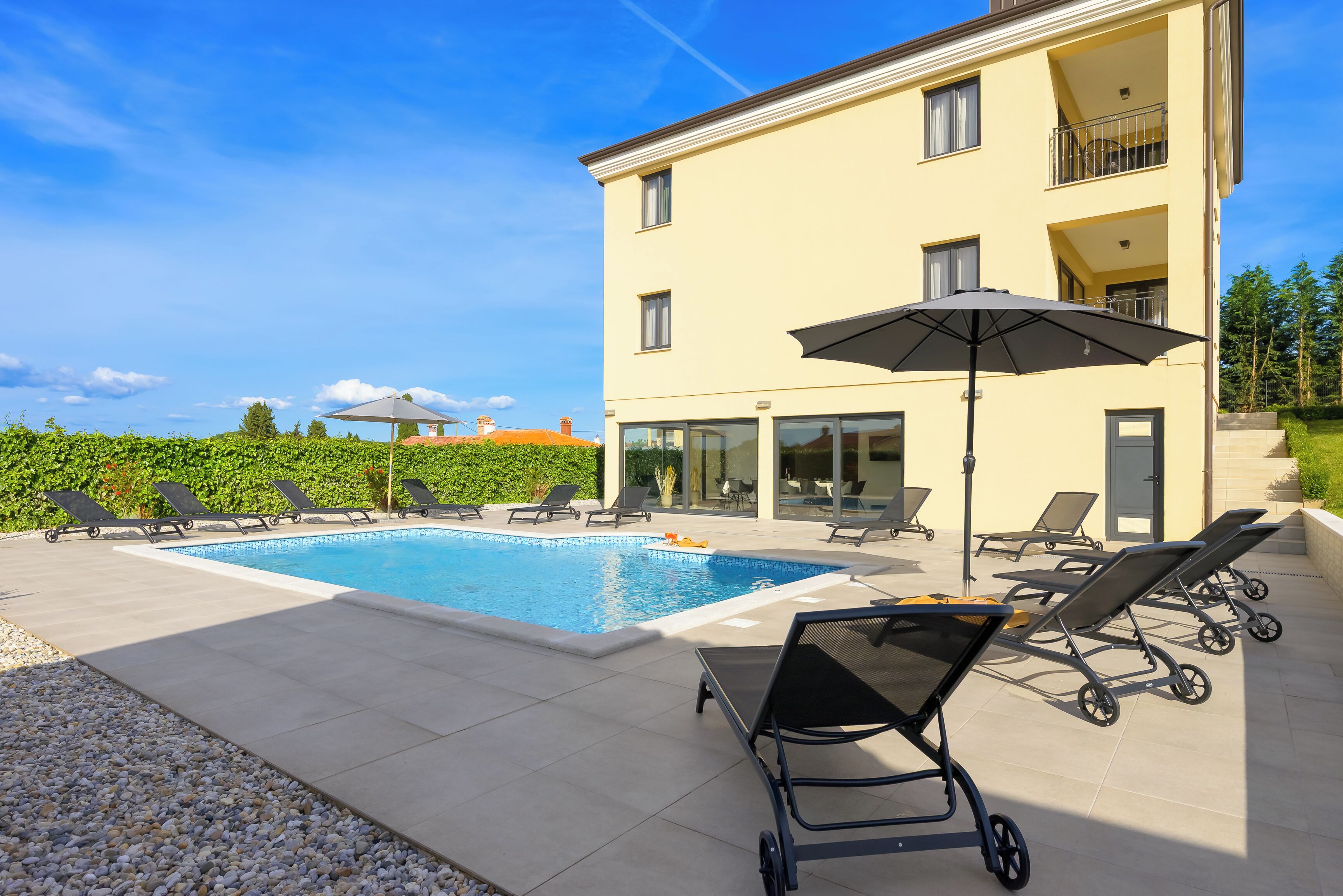 A pool area with lounge chairs, a large umbrella, and a building with balconies.