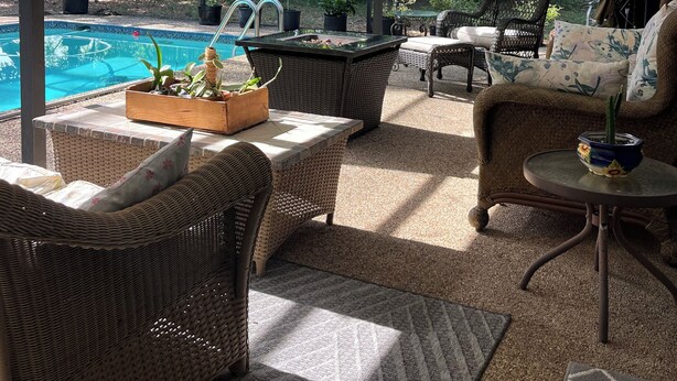 Een overdekt terras met rieten meubilair, een zwembad en een plafondventilator.