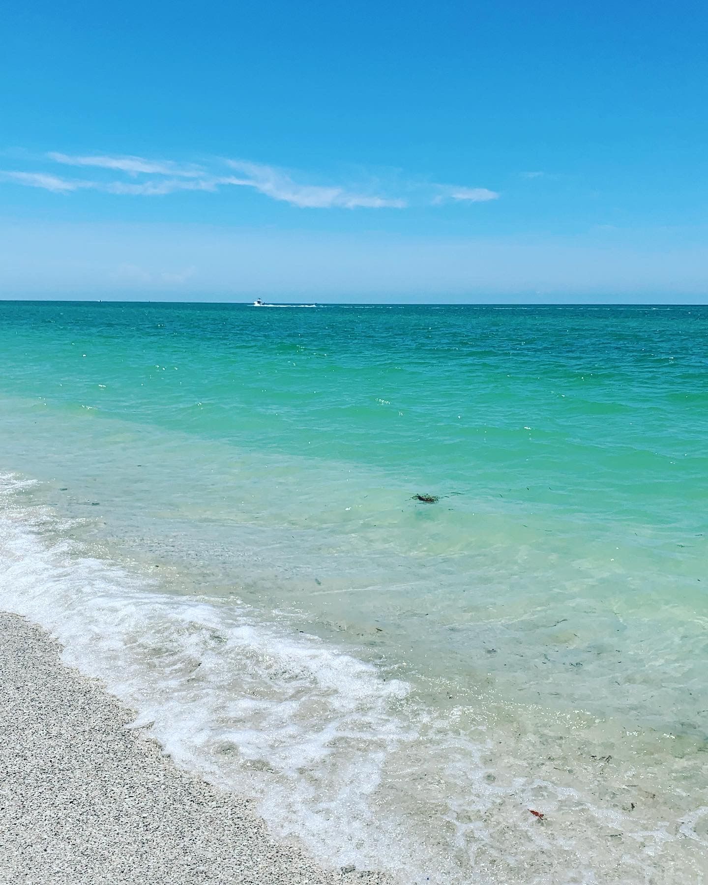 Une plage à l’eau turquoise et limpide, avec de douces vagues et un bateau qui se profile à l’horizon.