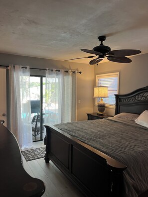 A bedroom with a bed, a ceiling fan, a window with blinds, a lamp, and a view of the outdoors. - Charming 3-bedroom house with a pool on one acre! 10% monthly discount. (Fort Myers)
