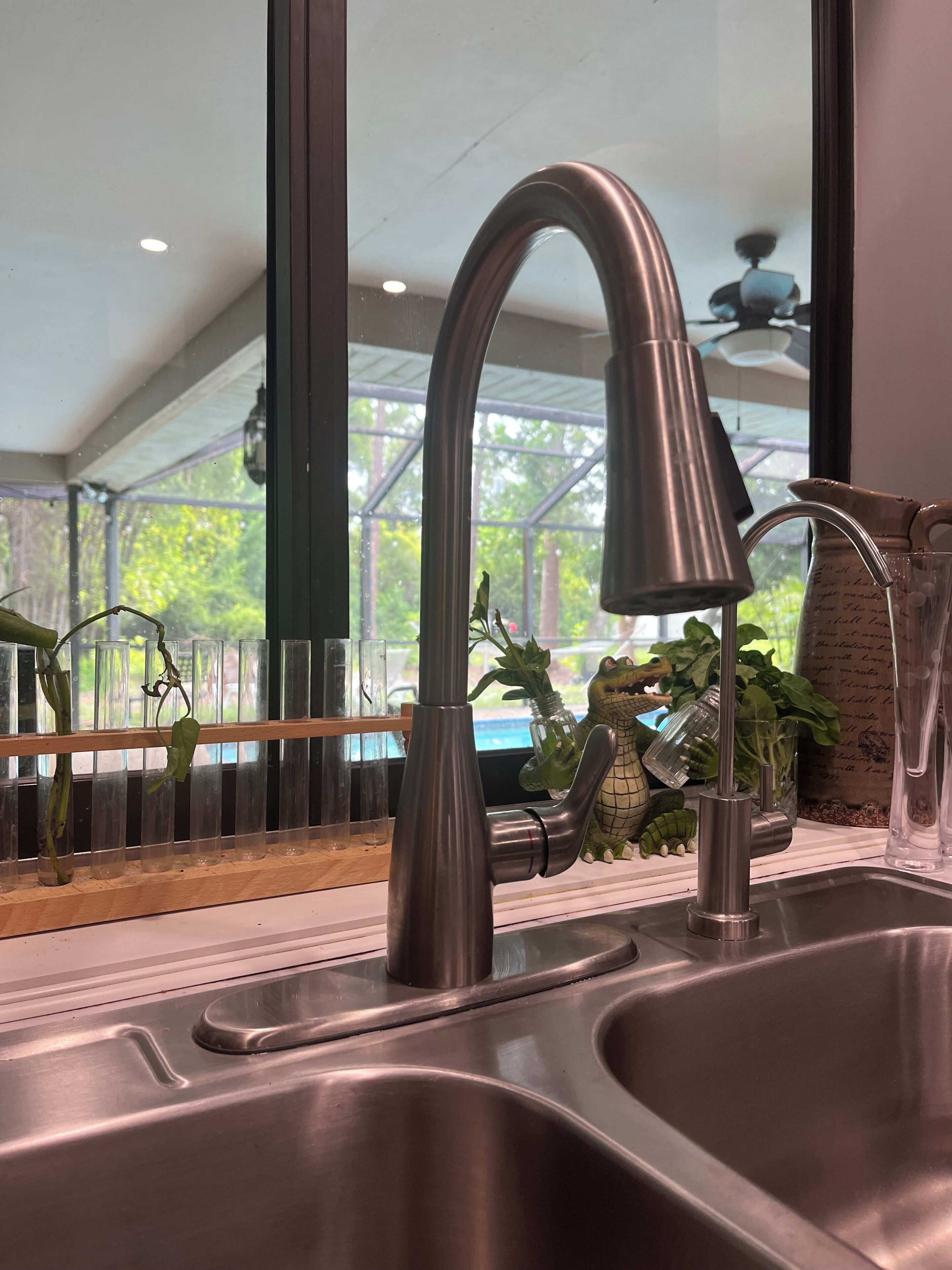 Una cocina moderna con un lavamanos de acero inoxidable, un grifo curvo y una ventana con vistas a follaje.