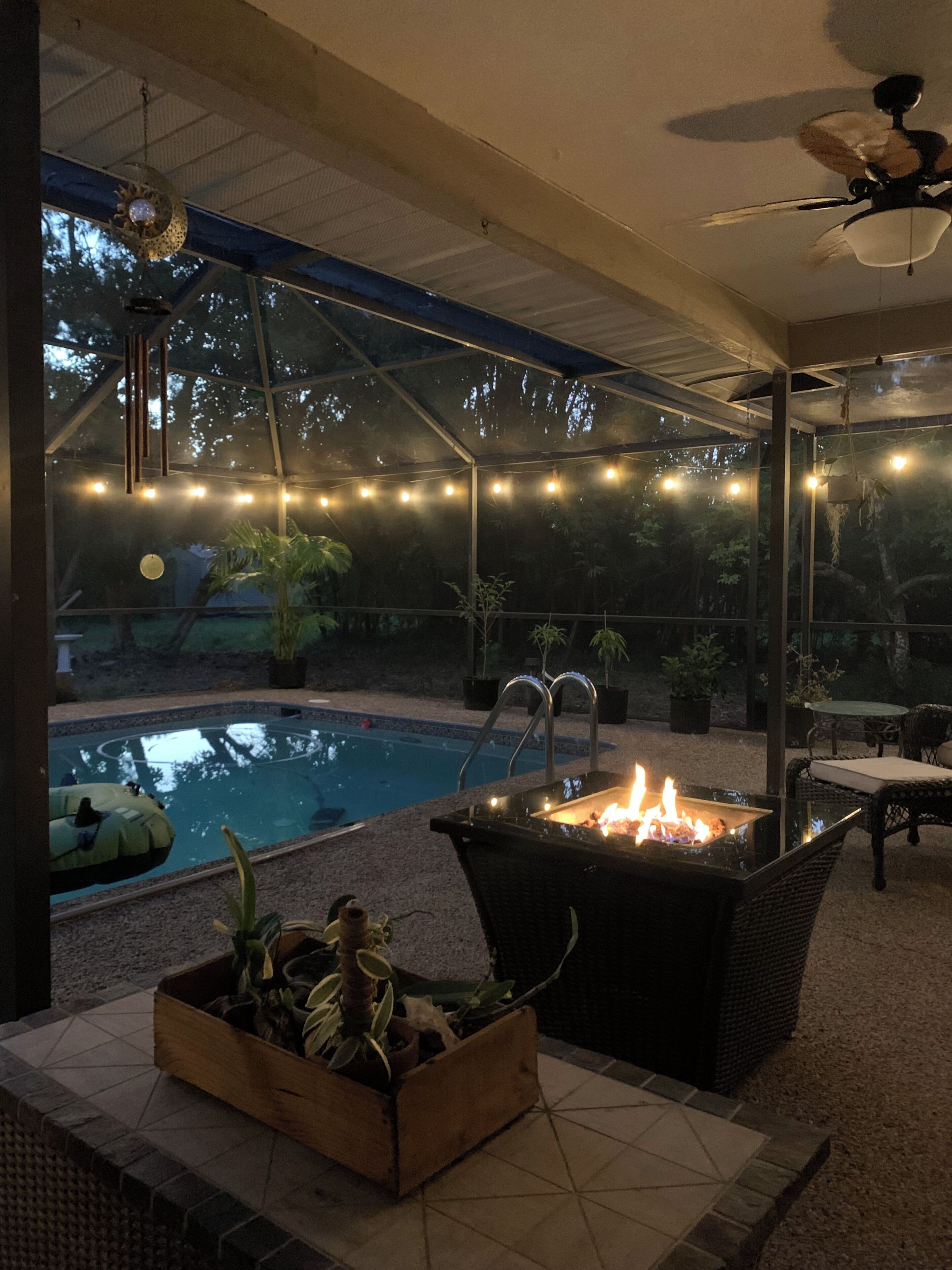 An outdoor patio area with a pool, a fire pit, and string lights.