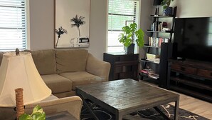Een woonkamer met een bank, salontafel, televisie, boekenkast en potplanten.
