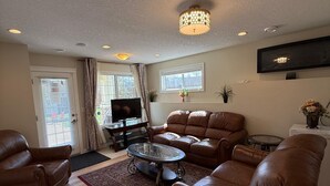 A living room with leather sofas, a glass coffee table, a flat-screen TV, and recessed ceiling lights. - 2 Bed Room, 1 Bath, Living, Kitchen, Office, Bright, Walkout Basement Suite (Calgary)