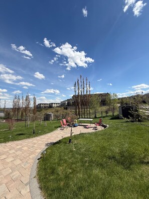 A paved pathway leading to a patio area with outdoor seating and a view of residential buildings in the background.